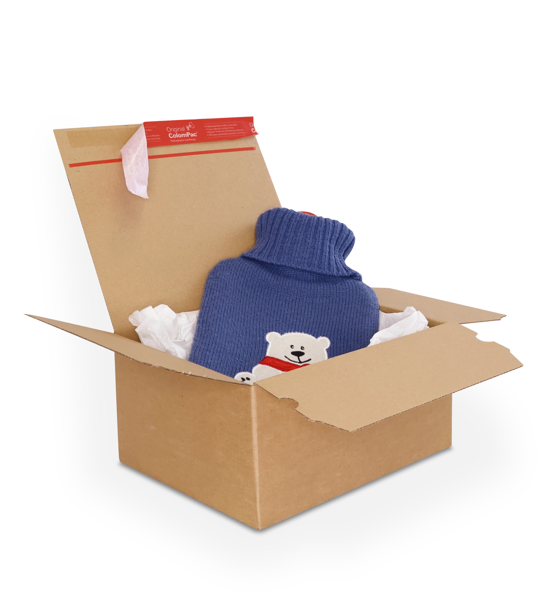Geöffneter brauner Versandkarton aus Wellpappe, darin liegt eine blaue Wärmflasche mit gestricktem Überzug, der einen weißen Bären mit rotem Schal zeigt. Der Karton ist teilweise mit weißem Seidenpapier ausgekleidet. Auf der oberen Klappe ein roter ColomPac-Selbstklebeverschluss.