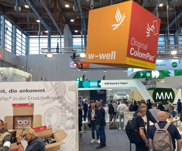 Messehalle mit ColomPac®-Stand zur Ersatzteillogistik; orangefarbener Würfel mit „w-well“ oben sichtbar.